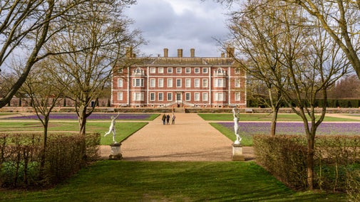 View from the tree-filled Wilderness towards Ham House with crocuses on the grass Plats